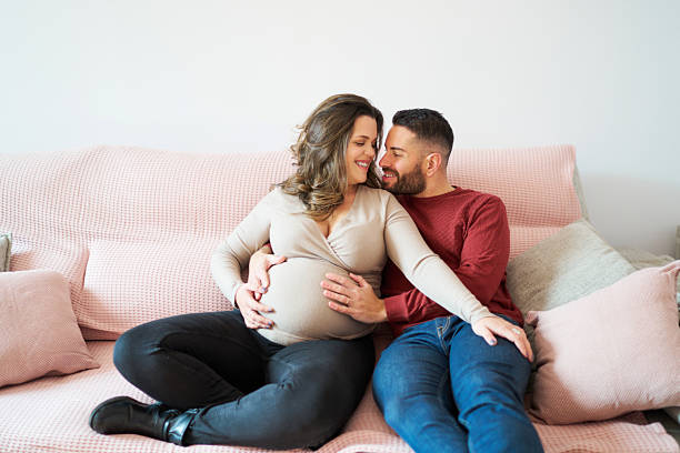 istock Expecting couple sitting on sofa embracing pregnant belly 2241644422