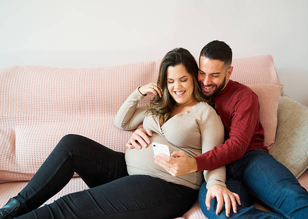 istock Pregnant couple sharing smartphone on couch at home 2241644449