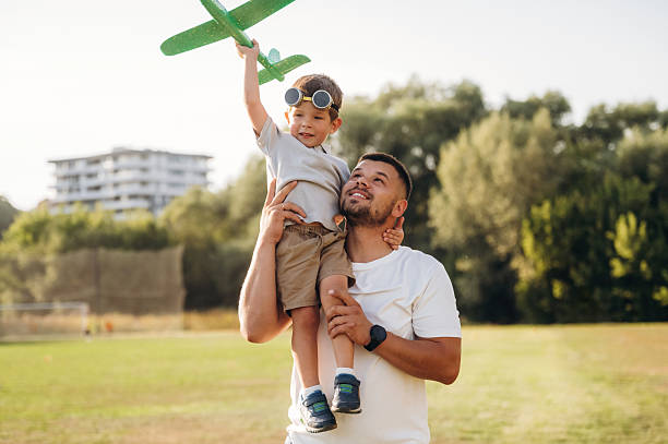 istock Toy plane in hand. Dad is holding son, having fun on the field 2241644501