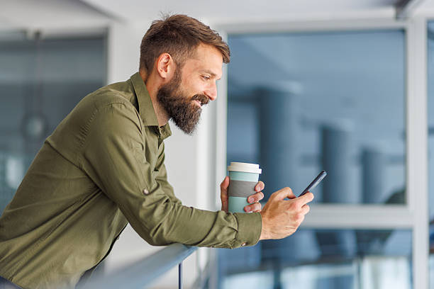 istock Smiling man telecommuting with coffee and smartphone on break 2241647136