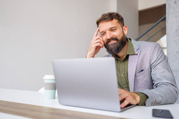 istock Bearded businessman smiling working on laptop in modern office 2241647220