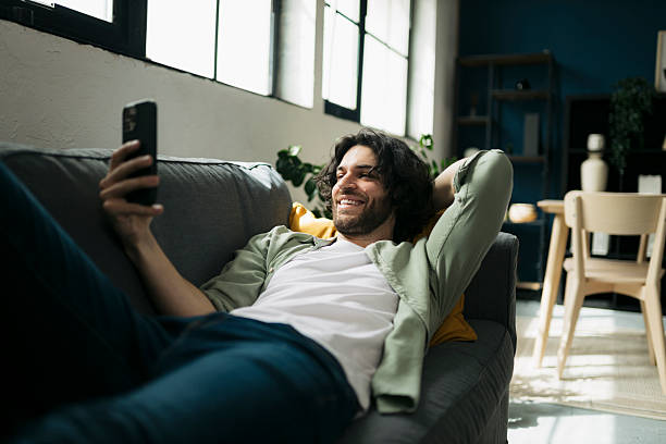 istock Cheerful man lying on couch and using mobile phone at home 2241647236
