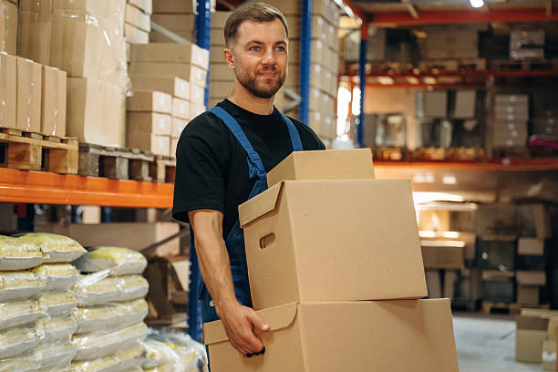 istock Blue uniform. Holding the box. Man is working in the storage with packages for shipment 2241648444