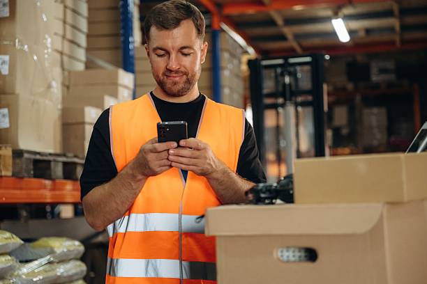 istock Time for a break, using smartphone. Man in uniform is working in the storage with packages for shipment 2241648979