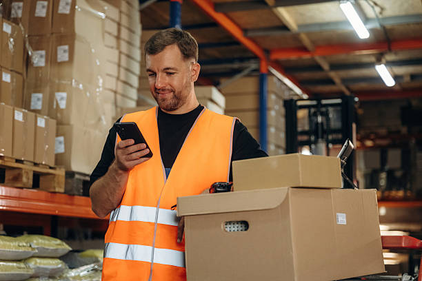 istock Time for a break, using smartphone. Man in uniform is working in the storage with packages for shipment 2241648989