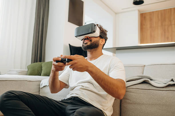 istock Virtual reality glasses, controller in hands. Man is in the modern domestic room at home 2241650256