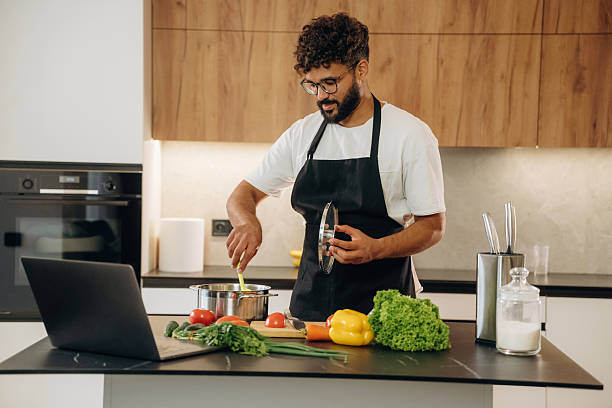 istock In black apron. Handsome man is preparing food on the kitchen 2241650379