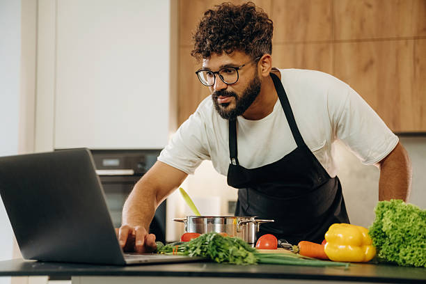 istock Taking online lessons, using laptop. Handsome man is preparing food on the kitchen 2241650399