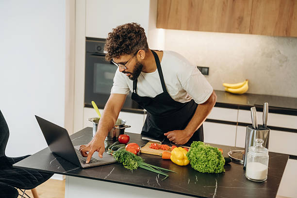 istock Taking online lessons, using laptop. Handsome man is preparing food on the kitchen 2241650435