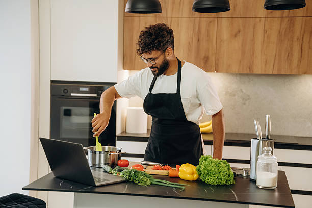 istock Taking online lessons, using laptop. Handsome man is preparing food on the kitchen 2241650448