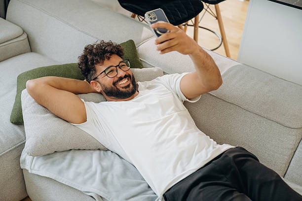 istock Data in the smartphone, holding it in hand. Man is lying down on the sofa at home, relaxing, feeling good 2241650771