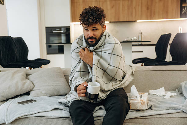 istock Warm tea in the cup. Sick man is on the sofa at home, with towel, feeling bad 2241651081