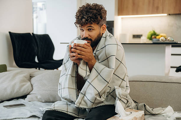 istock Warm tea in the cup. Sick man is on the sofa at home, with towel, feeling bad 2241651096