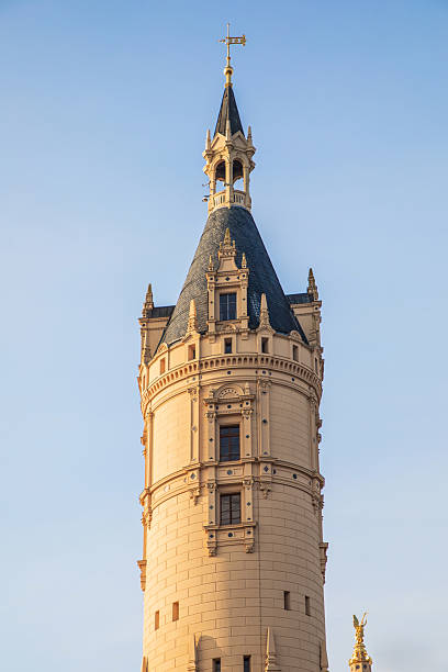 Schwerin, Mecklenburg-Western Pomerania - July 30, 2024: A woman and a man are standing on the lakeshore and looking at Schwerin Castle. The man is holding up a cell phone and taking a photo of the castle. It is a sunny day with a blue, cloudless sky.