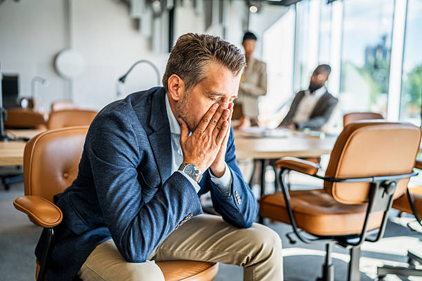 istock Stressed businessman covering face in busy office 2241652720