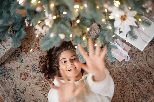 Woman lying under a decorated Christmas tree, reaching up.