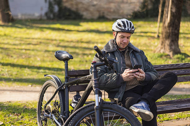 istock Man Checking Smartphone Resting on Park Bench Next to Bike 2241663860