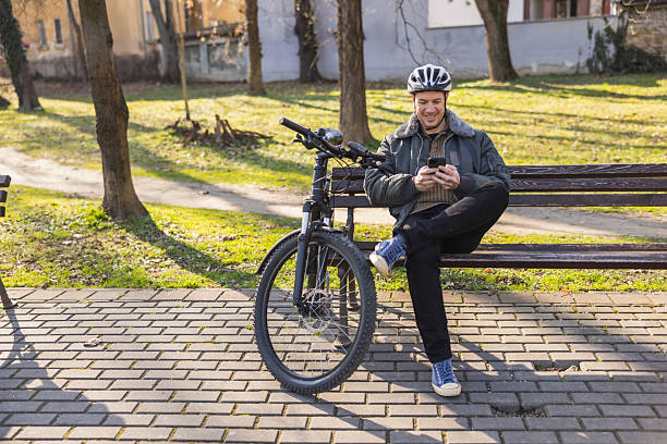 istock Man Checking His Smartphone While Sitting on a Park Bench Beside a Bicycle 2241663872