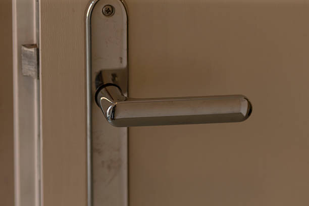 closeup metal door handle on wooden door, soft warm light highlights brushed finish and subtle scratches, modern lever style, focus on lock mechanism and hinge, ambient residential interior mood