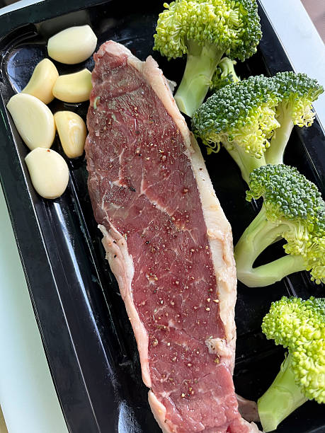 Raw beef steak fresh broccoli garlic clove black pepper cooking prep raw meat green vegetable food ingredient home kitchen natural light