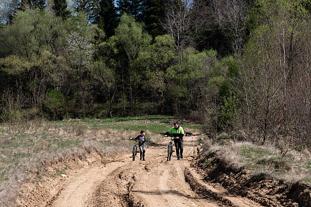 istock Father and son walk their bikes down a dirt road, surrounded by trees. 2241675014