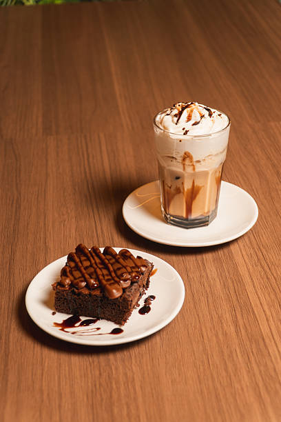 A chocolate brownie with a coffee milkshake on a wooden table.