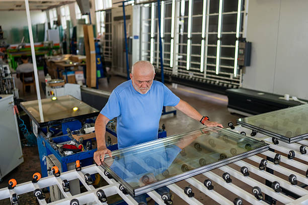istock An elderly worker controls the process of installing glass in PVC frames. 2241682431