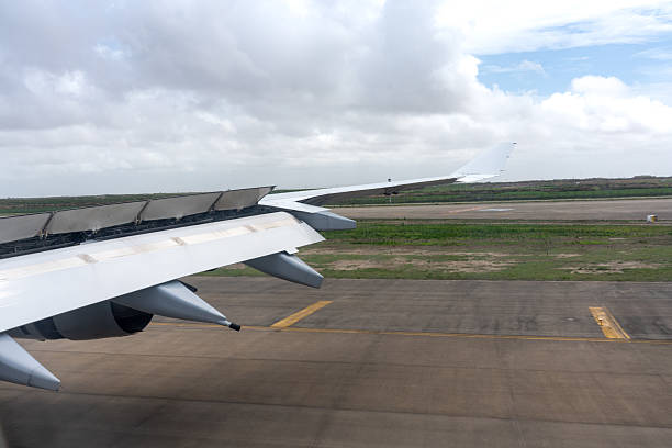 The aircraft wing shows its flaps deployed while approaching the runway. The scene emphasizes the mechanism and aviation logistics just before touchdown under a bright, cloudy sky.