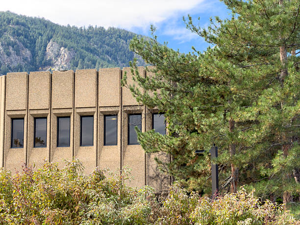 Concrete brutalist building standing against a mountain background with trees and bushes in the foreground
