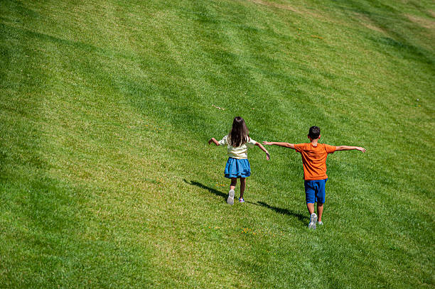 Brothers and sisters are running around and rolling on grass in a public park