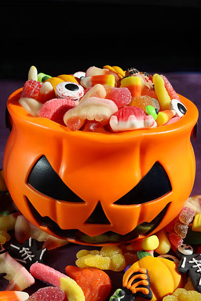 istock Full frame image of plastic, orange Jack O'Lantern pumpkin sweet collection bucket, trick or treat container full of gummy sweets, sweet and sour jellied candy, candy corn, black background, focus on foreground 2241691230