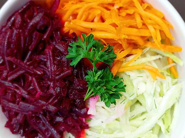 A vibrant salad displays shredded red beet, carrot, and cabbage topped with fresh parsley, showcasing a blend of colors and textures that is appetizing.
