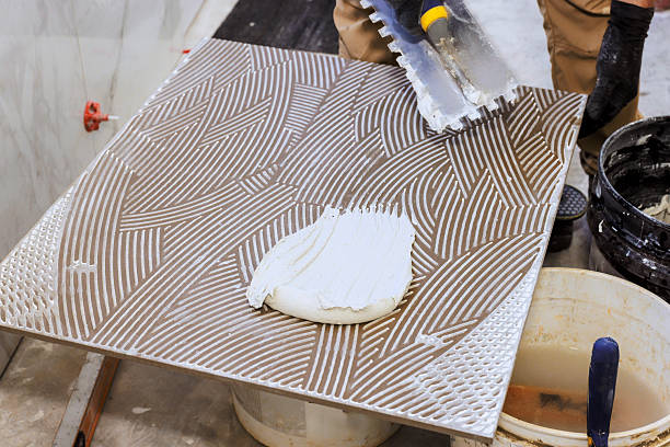 istock Worker applying adhesive to tile before installation at construction site during works daytime 2241698311