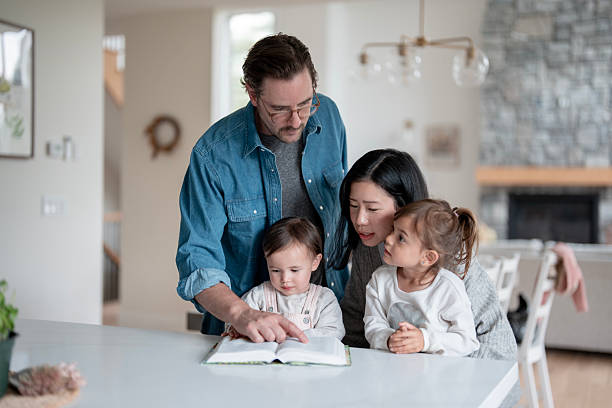 istock Family Reads Together At Kitchen Table As Father Points To Book While Asian Mom Looks On 2241709084