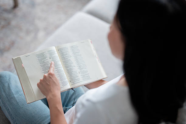 istock Asian Woman Reading Open Book While Relaxing On Couch In Casual Home Setting 2241709147