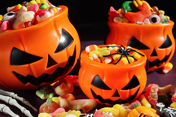istock Full frame image of three plastic, orange Jack O'Lantern pumpkin sweet collection buckets, trick or treat containers full of gummy sweets, surrounded by spilled sweet and sour jellied candy, candy corn, skeletal hand, spider, purple and black background 2241709517