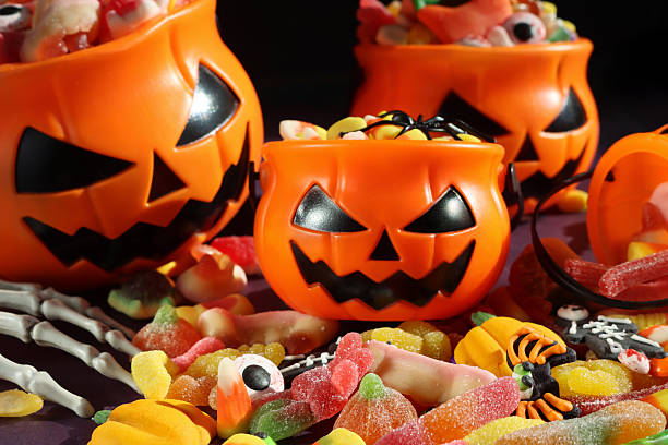 istock Full frame image of four plastic, orange Jack O'Lantern pumpkin sweet collection buckets, trick or treat containers full of gummy sweets, surrounded by spilled sweet and sour jellied candy, candy corn, skeletal hand, spider, purple and black background 2241709661