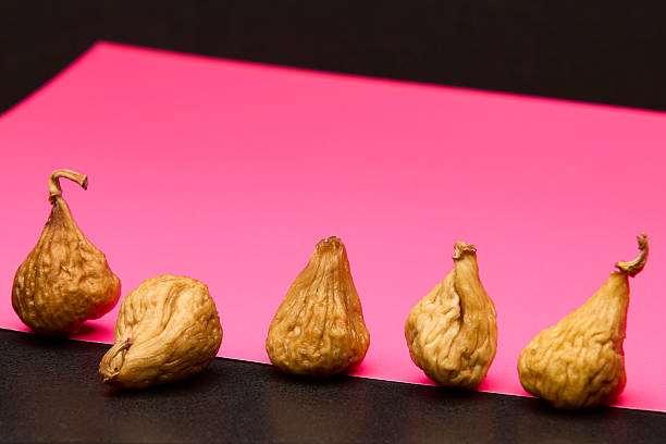 Studio image of several dried figs arranged in a row on vivid pink background. Creative composition highlighting textures and color contrast ideal for health and vegan food design.