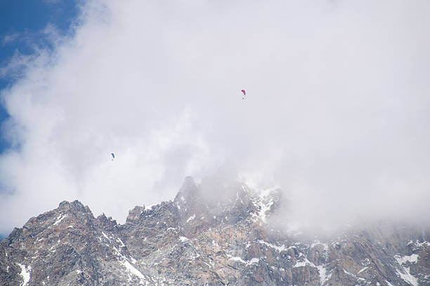 Colorful paragliders flying high over misty jagged mountains in the Alps