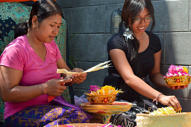 istock Balinese mother cuts ceremonial patterns as daughter decorates with flowers 2241742970