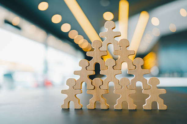 istock Wooden human figures stacked in pyramid shape on table with modern office background, symbolizing teamwork, leadership, collaboration, and organizational structure. 2241749666