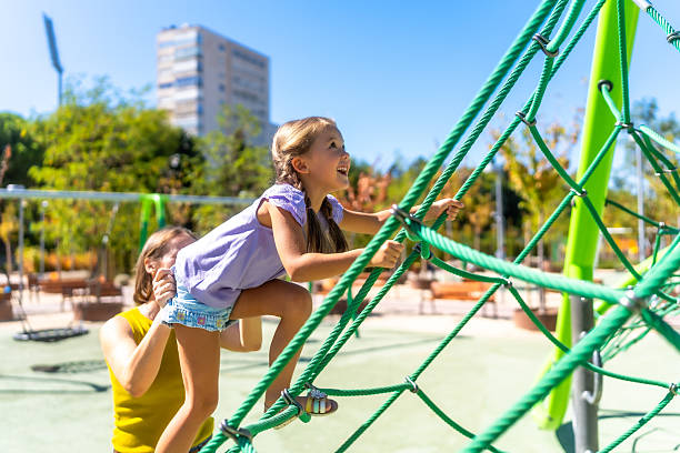 istock Mother helping daughter climbing rope net on playground 2241750620