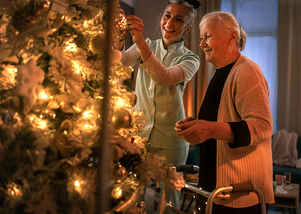 caregiver helping elderly woman decorate Christmas tree, viewed throught window