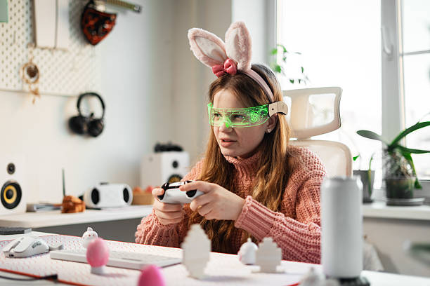 istock Young girl with bunny ears enjoys gaming in cozy Easter themed setup. Pastel colored eggs decorate desk, adding festive mood to virtual adventure. Holiday spirit and modern entertainment. 2241761837