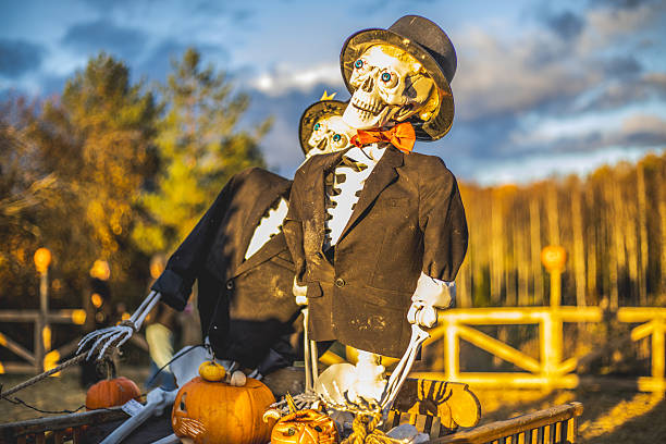 A jack o'lantern sits atop a scarecrow that stands in a group of pumpkins as a full moon risies in the distance.