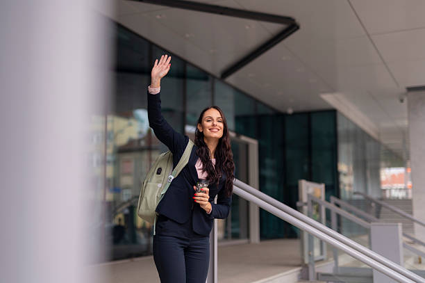 istock Smiling businesswoman waving while standing outside modern office building. 2241762054
