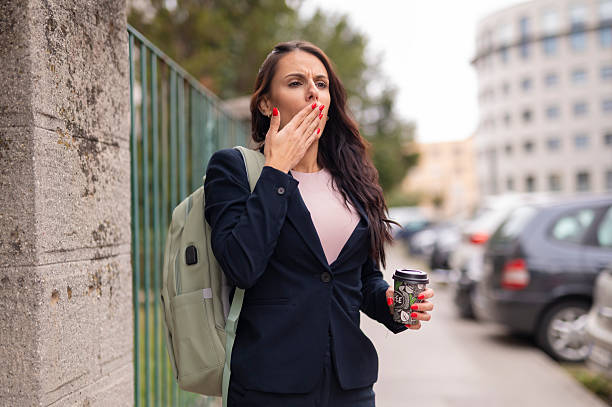 istock Businesswoman yawning while walking outdoors with coffee cup 2241762109
