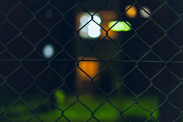 Out-of-focus apartment lights viewed through a wire fence at night in Japan. The soft bokeh and shadows create a quiet, cinematic urban mood.