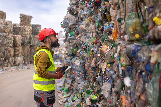 istock Worker Wearing Safety Gear Inspecting Large Compressed Plastic Waste Bales at Recycling Facility 2241768778