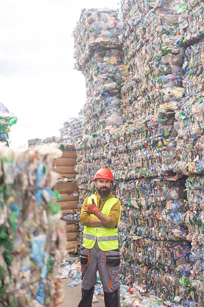 istock Male Worker Standing Among Large Compressed Plastic Waste Bales at Recycling Facility 2241768784